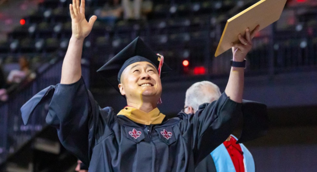 master's graduate holding hands up to the sky 